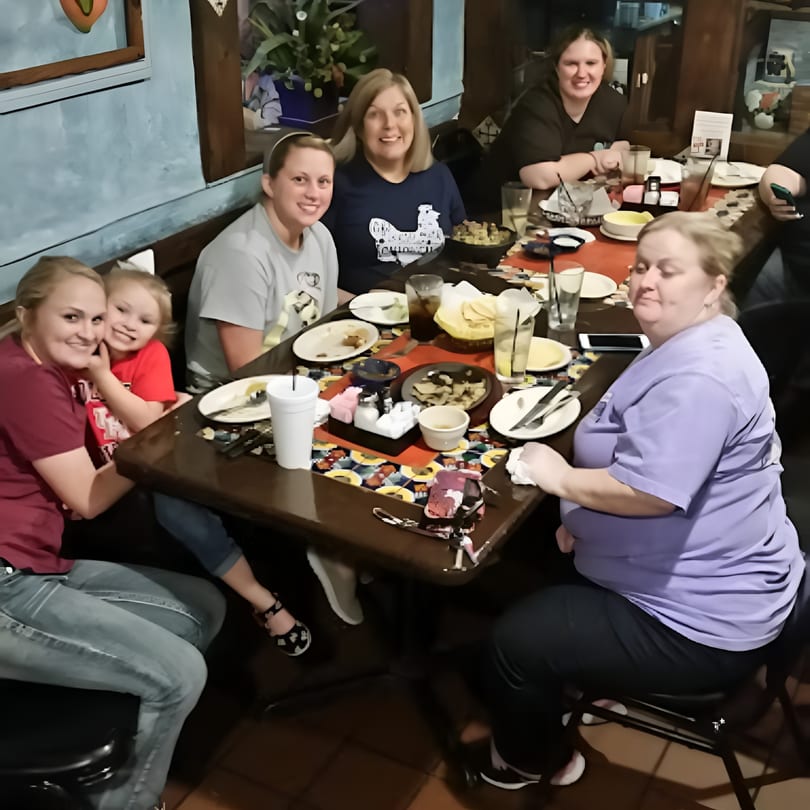 Six women and one child smiling and dining together at a restaurant table with food and drinks.