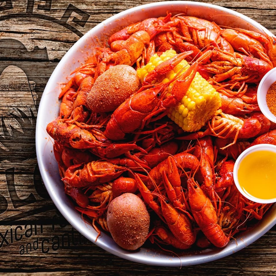 A large platter of bright red boiled crawfish, corn on the cob, and potatoes with dipping sauces.