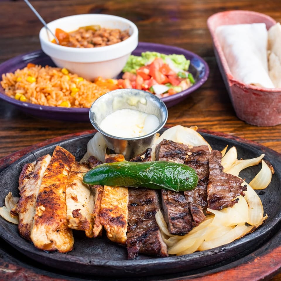 Sizzling fajitas with chicken, steak, onions, and a jalapeño, served with rice, beans, and salsa.