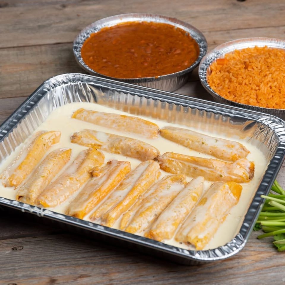 Chicken enchiladas in a foil pan with a side of rice and beans on a wooden table.