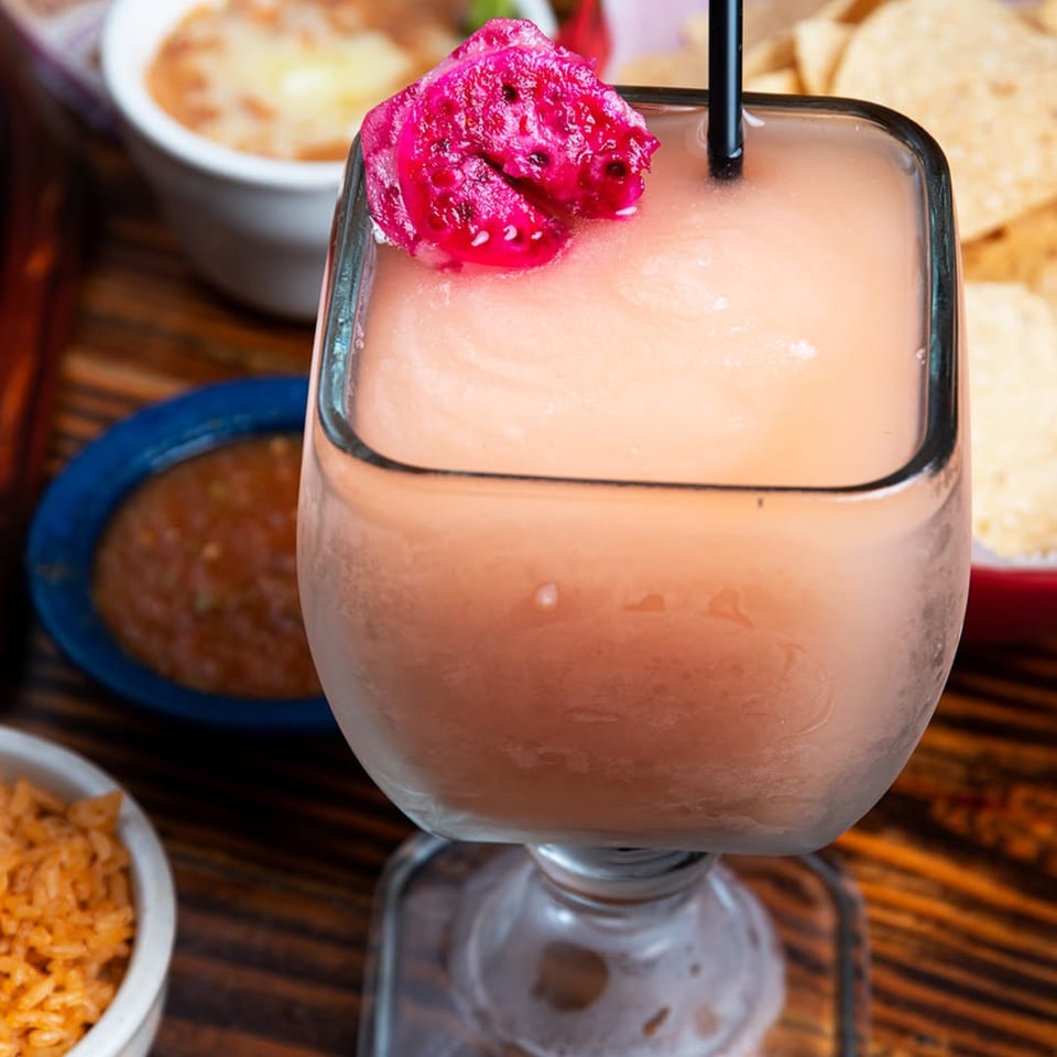 A frosty margarita with a black straw and a vibrant pink dragon fruit garnish.